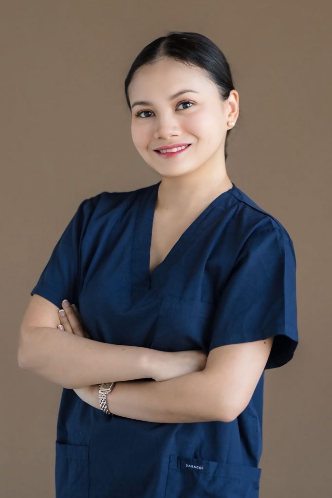 Portrait of Dr Hannah Nazri in navy medical scrubs standing with her arms crossed and smiling.